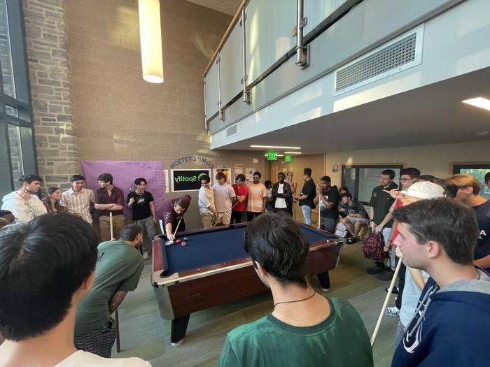 students gathered around pool table playing